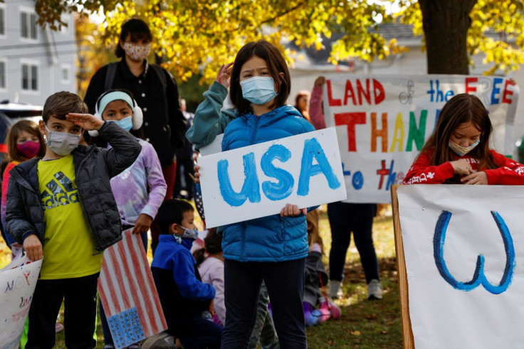 Anak-anak mengenakan masker pelindung berdiri memegang tanda selama upacara Hari Veteran di John Philip Sousa Memorial Bandshell di Sunset Park di Port Washington, New York, AS 11 November 2021.