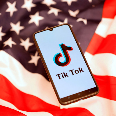Logo TikTok ditampilkan di smartphone sambil berdiri di atas bendera AS dalam ilustrasi ini
