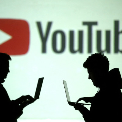 Siluet pengguna perangkat seluler terlihat di samping proyeksi layar logo Youtube pada ilustrasi gambar ini