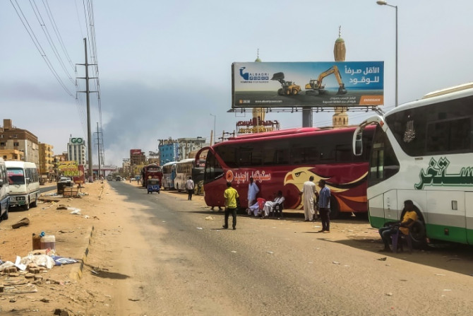 Asap mengepul di kejauhan saat orang-orang menunggu di sebelah bus penumpang di ibu kota Sudan, Khartoum