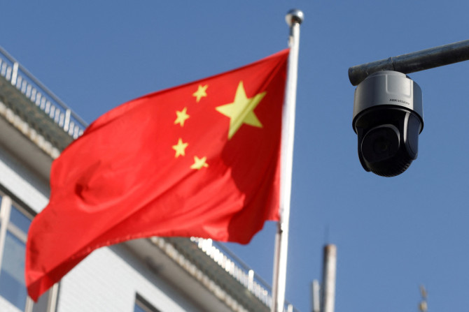 Sebuah kamera pengintai keamanan yang menghadap ke jalan digambarkan di sebelah bendera China yang berkibar di dekat Beijing