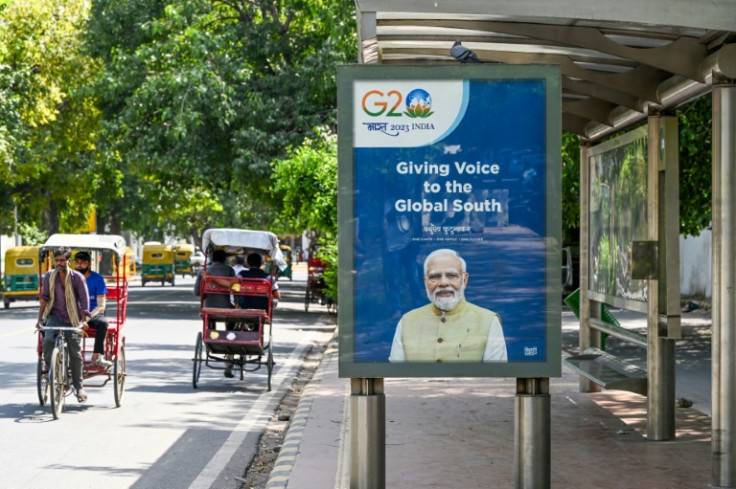 Orang-orang naik becak di dekat halte bus yang memajang poster G20 dengan potret Perdana Menteri India Narendra Modi, di New Delhi