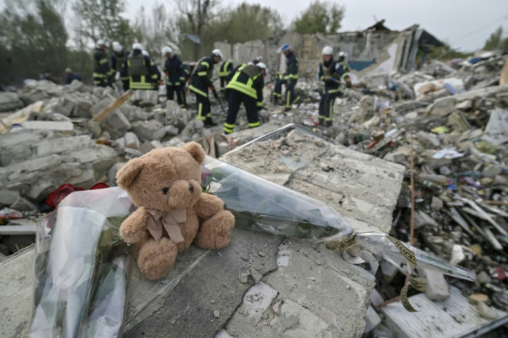 Sebuah boneka beruang dan bunga dipajang di pecahan tembok di desa Groze di mana lebih dari 50 orang tewas akibat serangan rudal.